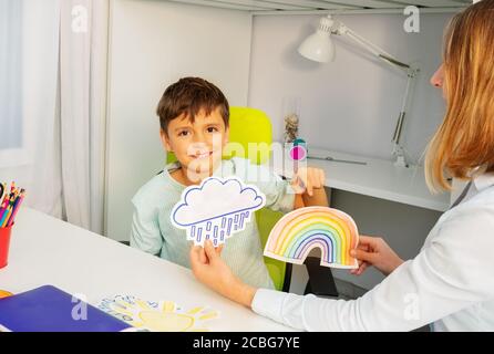 Bambino durante la terapia di sviluppo di aba che si siede selezionando fra due carte di arcobaleno e tempesta Foto Stock