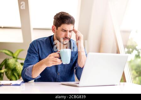 Scatto di un uomo d'affari con gli occhi chiusi e le mani sul tempio, mentre si siede dietro il suo laptop e soffre di forte dolore alla testa. Foto Stock