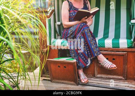 donna in estate abito rilassante in sdraio sul ponte o patio che legge un libro Foto Stock