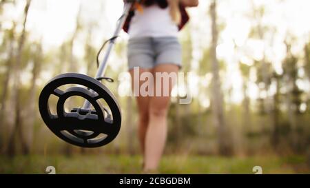 Donna cacciatore di tesori con rivelatore di metalli piano di scansione in foresta. Scatto ad angolo basso. Foto di alta qualità Foto Stock