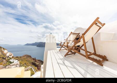 Rilassati a Santorini. Vista sulla caldera e sul mare dal balcone, Santorini, Grecia. Terrazza bianca del resort con concetto di chaise lounge. Mattina nuvolosa a Oia. Foto Stock