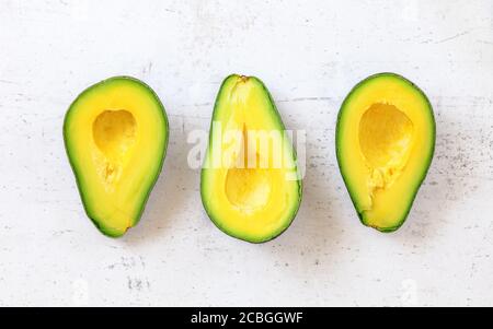 Vista dall'alto verso il basso, tre metà di avocado su tavola da lavoro bianca. Foto Stock