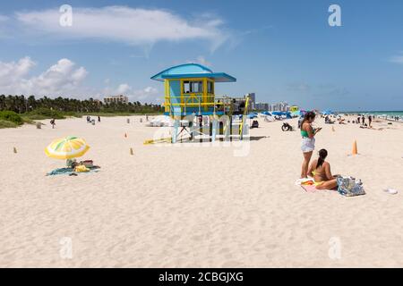 Le persone che si godono una giornata sulla spiaggia con uno stand bagnino sullo sfondo, a South Beach, Miami Beach, Florida, USA. Foto Stock