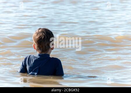 una vista ravvicinata di un piccolo ragazzo che galleggia dentro l'acqua poco profonda nell'oceano Foto Stock