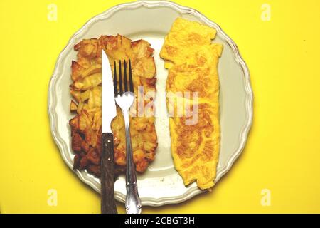 patate arrosto o fritte e omelette su un piatto verde con posate sulla parte superiore. concetto di cibo. piatto. Foto Stock