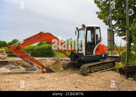 Escavatore cingolato compatto con piattaforma girevole e cingoli caterpillar continui su un cantiere di sostituzione delle fogne in Italia nord-occidentale Foto Stock