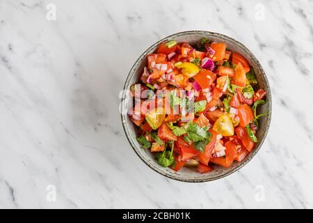 Tex Mex Pico de Gallo salsa di pomodoro. La salsa contiene pomodori, coriandolo e cipolla rossa. La ciotola è vista dall'alto, piatta su un dorso di marmo bianco Foto Stock