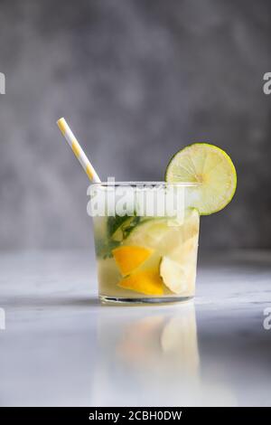 Cocktail o mocktail drink stile Caipirinha fatto con lime, ghiaccio, zucchero e un liquore di canna da zucchero. La bevanda è davanti a uno sfondo grigio su una marbl Foto Stock