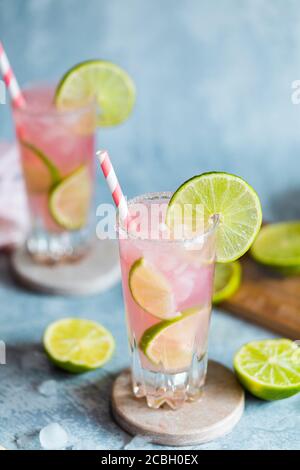 Due bicchieri di un cocktail o mocktail rosa fresco con succo di lime e pompelmo. Cocktail di Paloma, bevanda rosa. Con cannucce di carta. Sfondo grigio blu Foto Stock