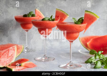 Tre bevande fresche e surgelate di margarita con fragole e cocomero. Le bevande sono guarnite con foglie di basilico e anguria. Grigio backgro Foto Stock