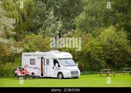 Uomo e donna seduti con una bevanda fuori dal loro motore camper a casa su un piccolo sito 5 van caravan Nel Thame Oxfordshire Foto Stock