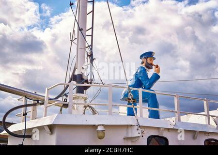 La figura del marinaio si siede sul ponte di una barca. Con cielo e nuvole sullo sfondo. Foto Stock