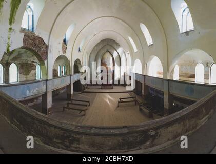 All'interno di un'antica chiesa abbandonata. Interno antico dell'edificio culto. Panchine e altare. Un'ampia croce in legno si trova nell'angolo. Vista dal sec. Foto Stock