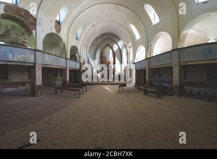 All'interno di un'antica chiesa abbandonata, antico interno di edificio religioso, panchine e altare, all'angolo si trova una croce di legno Foto Stock