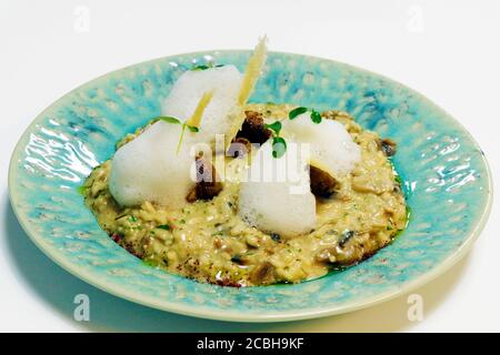 Risotto ai funghi, specialità di riso italiano con formaggio parmigiano croccante, schiuma ed erbe aromatiche Foto Stock