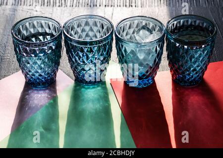 Quattro bicchieri d'acqua blu a motivi geometrici con ghiaccio o cocktail con lunghe ombre su carta colorata e sfondo nero. Foto Stock