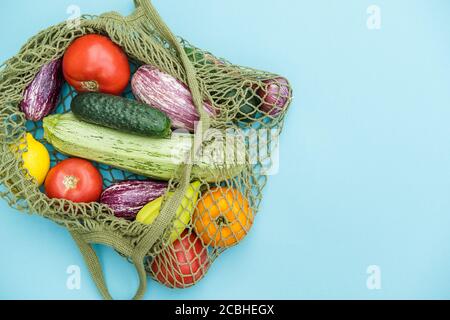 Borsa verde a corda con varie verdure fresche su sfondo blu. Zero rifiuti, verdure fresche in sacchi a rete riutilizzabili. Foto Stock