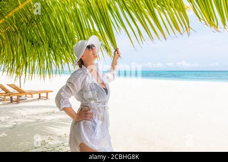 Donna che si rilassa sulla spiaggia, concetto di vacanza estiva, donna felice con abito bianco, cappello che si rilassa in amaca sulla spiaggia tropicale al tramonto Foto Stock