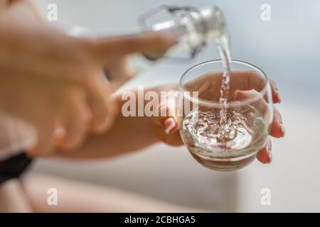 Versare acqua. Primo piano versare acqua fresca purificata dalla bottiglia sul tavolo su uno sfondo naturale sfocato Foto Stock