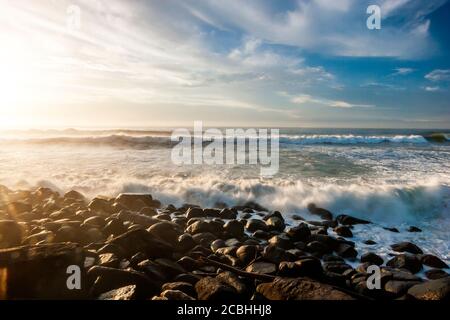 Onde oceaniche che si infrangono sulla spiaggia rocciosa Foto Stock