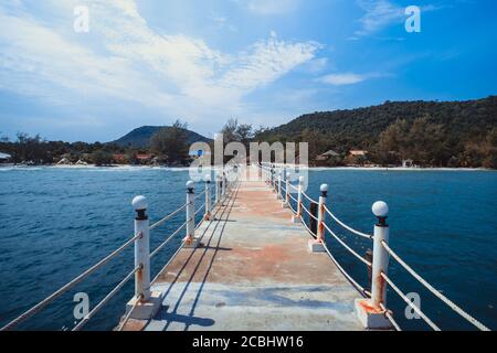 il ponte pier si estende dalla spiaggia al mare dalle onde turchesi. Cielo nuvoloso blu profondo dopo la grande tempesta. Aspettative per i sogni di successo, viaggi ed estate Foto Stock