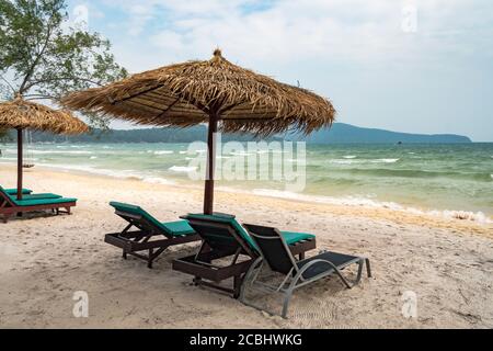 Spiaggia calma scena con lettini e ombrelloni di paglia sotto palme da cocco vicino al mare dei Caraibi. Paradiso tropicale con chaise lounges su sabbia bianca, no Foto Stock