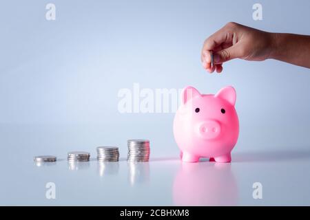 Mano di capretto che tiene moneta messo in banca piggy con pila di soldi crescente crescita che risparmia denaro, concetto di investimento per il piano di libertà finanziaria, business. Foto Stock