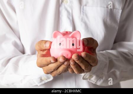 Mano di capretto che tiene moneta messo in banca piggy con pila di soldi crescente crescita che risparmia denaro, concetto di investimento per il piano di libertà finanziaria, business. Foto Stock