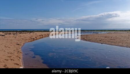 Un canale di Freshwater che attraversa la spiaggia sabbiosa di East Haven, un piccolo villaggio di pescatori sulla costa orientale della Scozia. Foto Stock