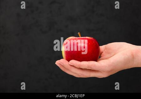 Mano femminile che tiene una mela matura rossa su sfondo nero. Primo piano. Spazio di copia Foto Stock