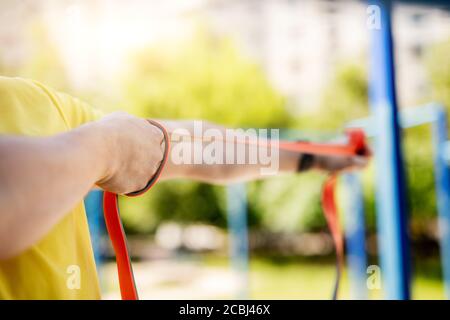 Uomo che si esercita con la fascia di gomma di resistenza in strada, primo piano Foto Stock