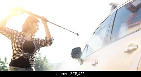 Donna che pulisce la finestra dell'automobile con acqua di getto durante il lavaggio dell'automobile Foto Stock
