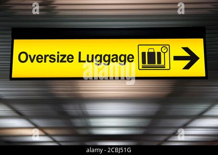 il cartello giallo del bagaglio oversize con la freccia si appende al soffitto in aeroporto Foto Stock