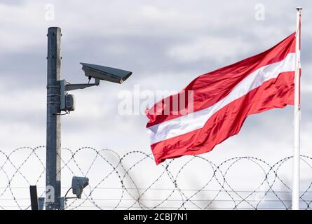 Bandiera lettone e confine con telecamera di sorveglianza e filo spinato, immagine concettuale Foto Stock