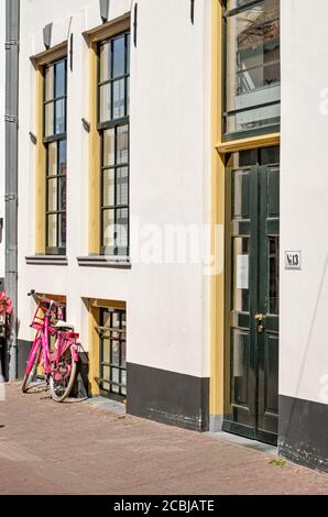 Hattem, Paesi Bassi, 31 luglio 2020: Facciata nel centro storico con intonaco bianco e cornici verdi e gialle e una bicicletta rosa Foto Stock