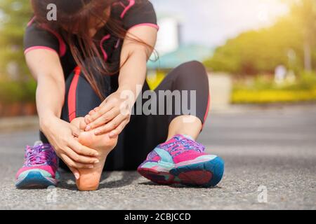 Atleta di corridore femminile lesioni ai piedi e dolore. Donna che soffre di piede doloroso mentre corre sulla strada. Foto Stock