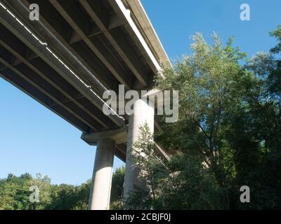 Multidy Lane Highway Bridge con colonne in cemento armato circondate da alberi vista dal basso. Sfondo blu cielo Foto Stock
