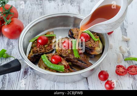 La donna sta versando la salsa di pomodoro nella padella per piatto di melanzane in cottura Foto Stock