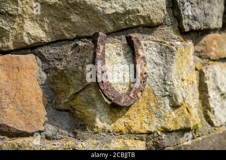 Un vecchio ferro di cavallo arrugginito proppato su una grande pietra. Simbolo di felicità e fortuna. Foto Stock