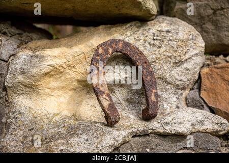 Un vecchio ferro di cavallo arrugginito proppato su una grande pietra. Simbolo di felicità e fortuna. Foto Stock