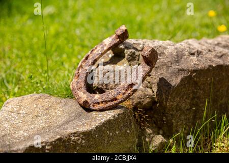Un vecchio ferro di cavallo arrugginito proppato su una grande pietra. Simbolo di felicità e fortuna. Foto Stock