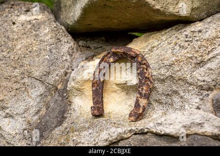 Un vecchio ferro di cavallo arrugginito proppato su una grande pietra. Simbolo di felicità e fortuna. Foto Stock