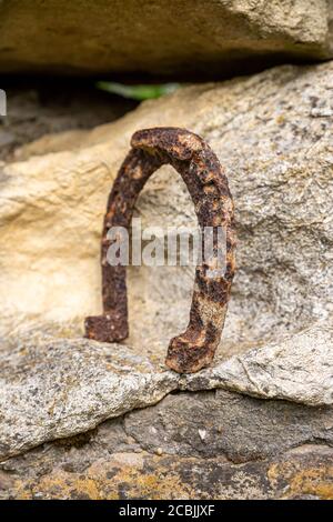 Un vecchio ferro di cavallo arrugginito proppato su una grande pietra. Simbolo di felicità e fortuna. Foto Stock