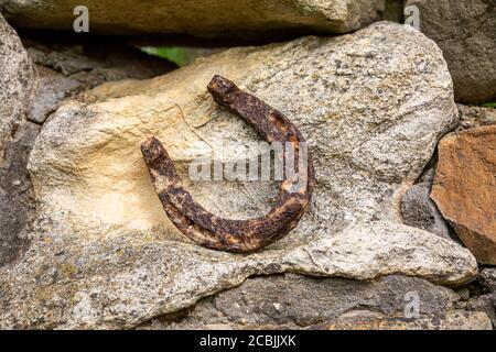 Un vecchio ferro di cavallo arrugginito proppato su una grande pietra. Simbolo di felicità e fortuna. Foto Stock