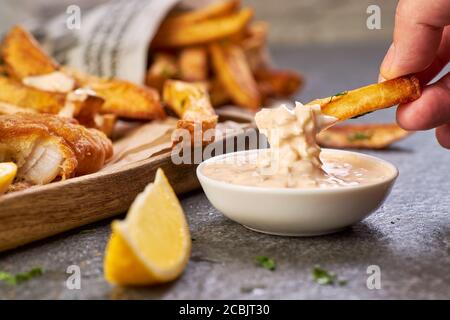 Tenere a mano una patatine fritte e immergerla in salsa tartaro Foto Stock