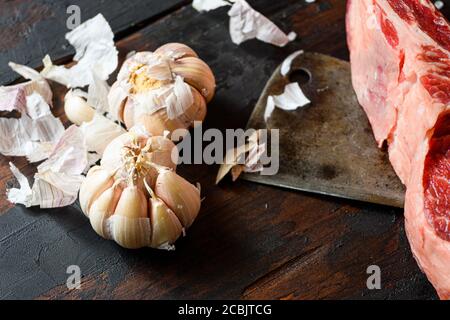 Aglio, che si trova vicino al coltello da taglio con carne di manzo cruda bistecca. Carne di manzo cruda preparata per cucinare le bistecche. Accanto agli ingredienti per cucinare Foto Stock