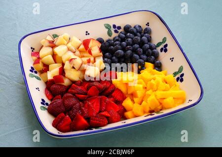 Un piatto di frutta sano con mango fresco, pesche e bacche Foto Stock