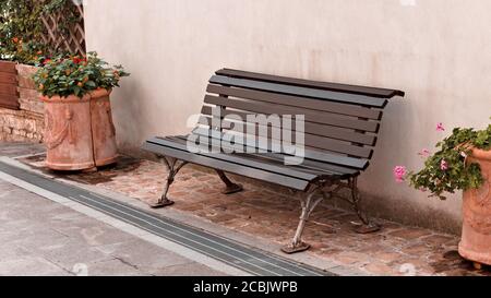 Panca nera isolata nel cortile vicino a due vasi con piante e fiori di fronte al muro (Italia, Europa) Foto Stock