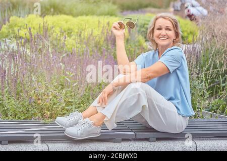 Attiva caucasica anziana signora 60 anni è a piedi dentro il parco pubblico e seduto sulla panchina segnata per distanza sociale durante il coronavirus covid-19 Foto Stock