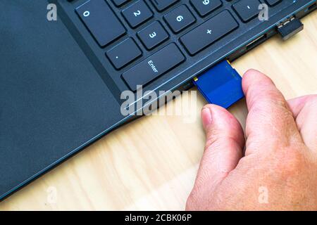 una mano dell'uomo che inserisce una scheda flash in un computer portatile connettore Foto Stock